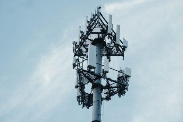 Nahaufnahme eines Mobilfunkmasts mit zahlreichen Antennen vor blauem Himmel