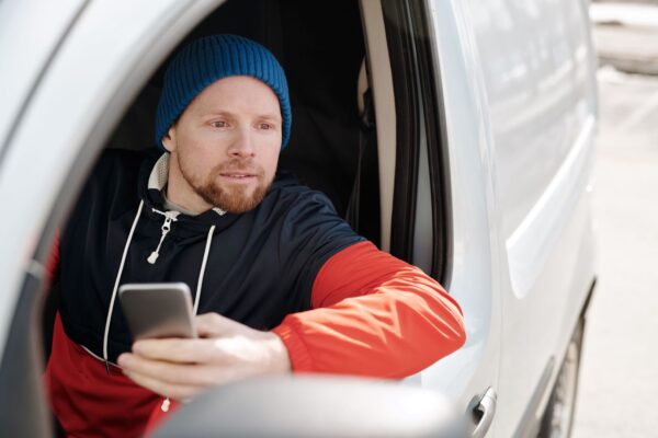 Mann mit Smartphone sitzt in einem Fahrzeug und blickt nach draußen