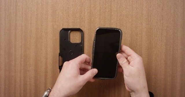 Hände setzen ein Smartphone in eine schwarze Schutzhülle ein
