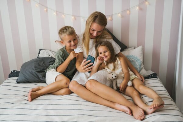 Mutter und zwei Kinder betrachten gemeinsam ein Smartphone im Bett