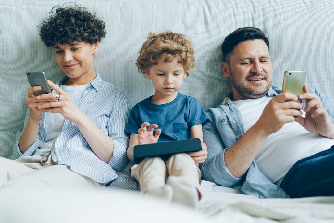 Familie mit zwei Smartphones und einem Tablet auf dem Sofa
